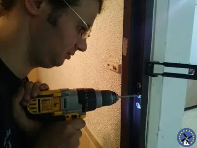 מנעולן קודח בקצה הדלת במקדחה להתאמת בית המנעול בעת ההתקנה