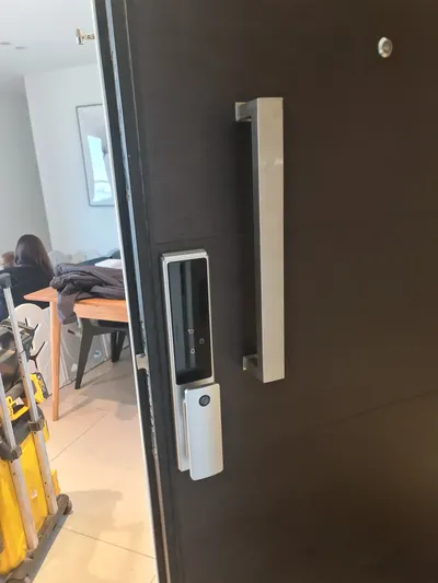 מנעול חכם Amsterdam כסף מותקן על דלת כניסה כהה עם ידית משיכה, לוח מגע וקורא טביעת אצבע