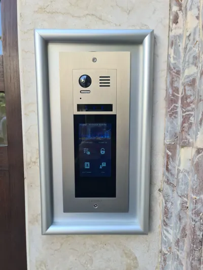 אינטרקום מסך מגע VisionNet מותקן בכניסת בניין, פאנל נירוסטה בקיר שיש עם מצלמה ומסך מגע פעיל בעברית